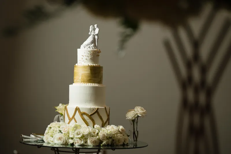 Tiered wedding cake with white tiers and gold painted chevron patterns is topped with a couple figurine and framed by white