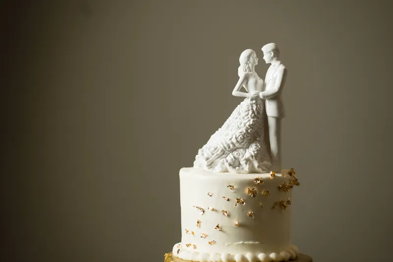 White wedding cake topped with a bride and groom figurine, accented with gold leaf details at Casa Monica Resort & Spa.