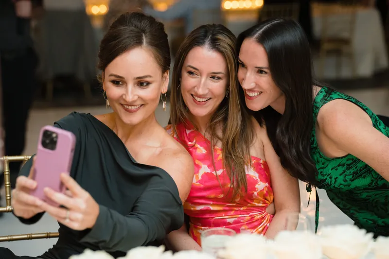 Three female guests smile while taking a selfie at the wedding reception.
