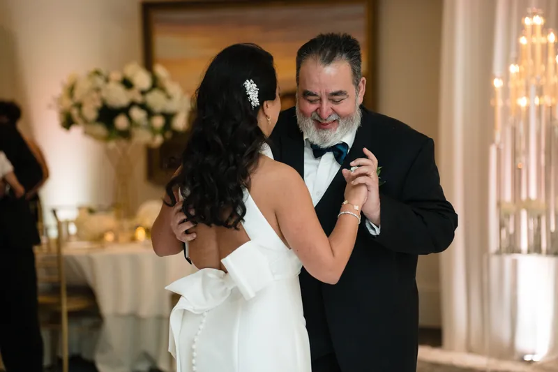 Cole holds a microphone while dancing with Lehna in a white dress at the reception.