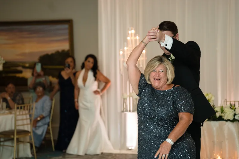 Cole dances with a guest in a sparkly gray dress while Lehna watches from across the ballroom.