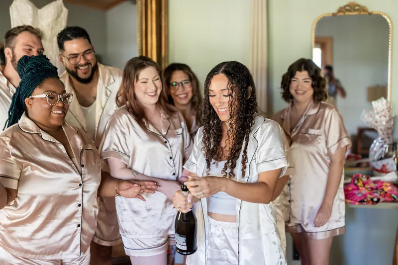 Lena and her bridesmaids laugh together in their satin robes during bridal preparations.