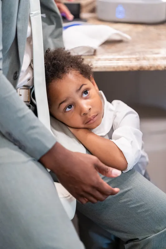 A young child rests against an adult's legs, looking up with a thoughtful expression during the wedding day.
