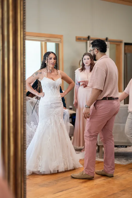 Lena in a white mermaid gown chats with Blake and another guest inside the venue's bridal suite.
