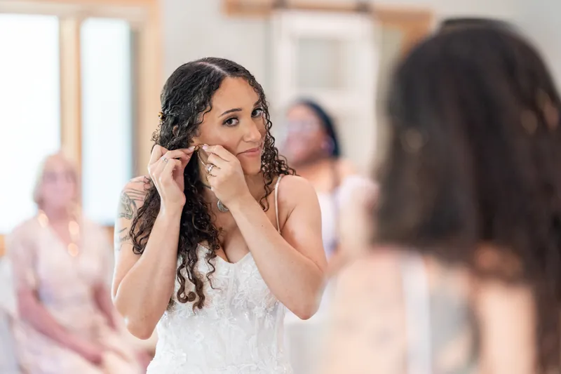 Lena touches her braided updo while standing in front of a mirror, preparing for the ceremony.