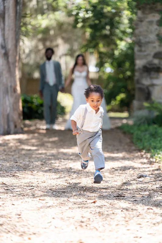 Their son runs ahead down a dirt path as Blake and Lena walk behind him, stone structures visible in the distance.