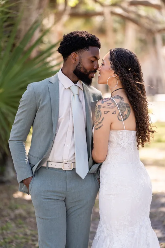 Lena leans toward Blake for a kiss under the oak canopy at Fountain of Youth Archaeological Park, her lace gown catching
