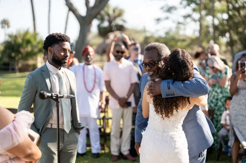 Blake watches with a smile as a guest hugs Lena immediately after their ceremony in the tree-lined park setting.