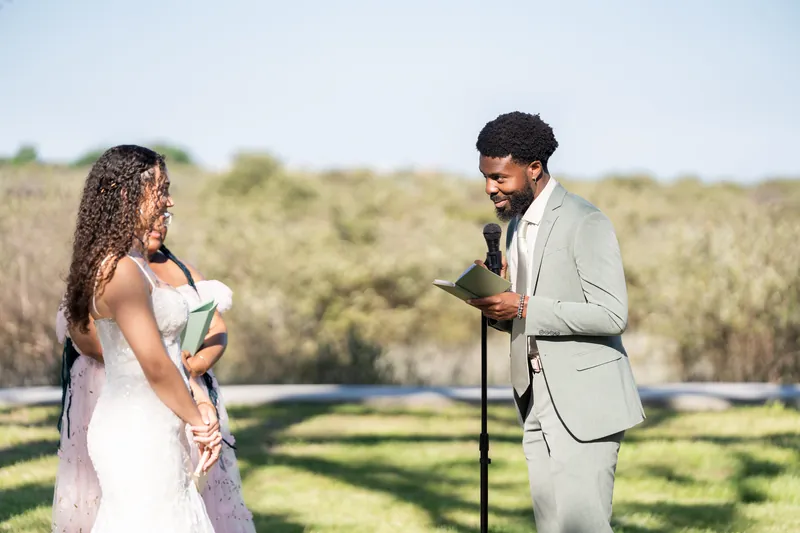 Lena listens intently as Blake speaks at the microphone during their outdoor reception ceremony.