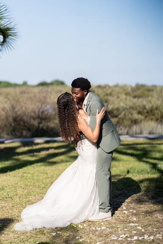 Blake kneels to embrace Lena after their first kiss, her long curled hair cascading over his shoulder as guests watch