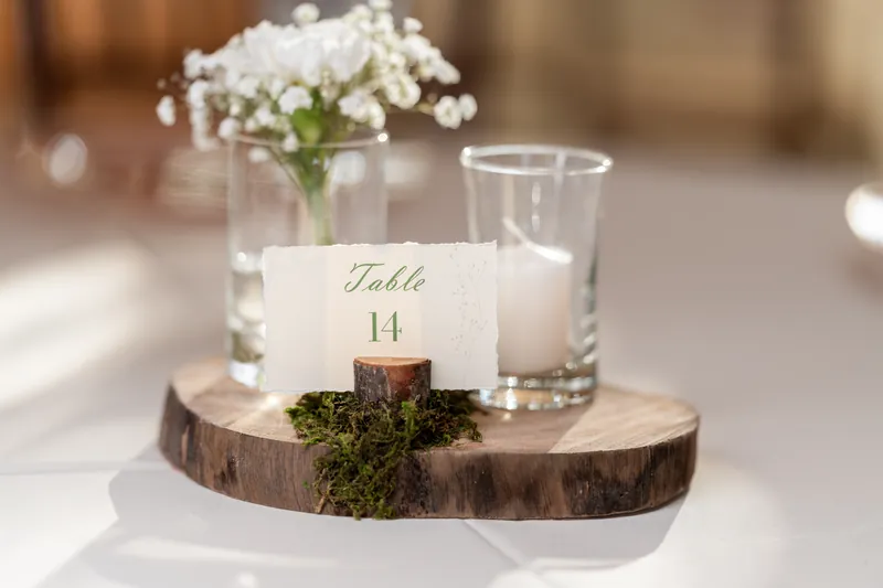 A wood-slice table holds a brass candle, baby's breath in glass, and a "Table 14" card for the reception at Fountain of Youth