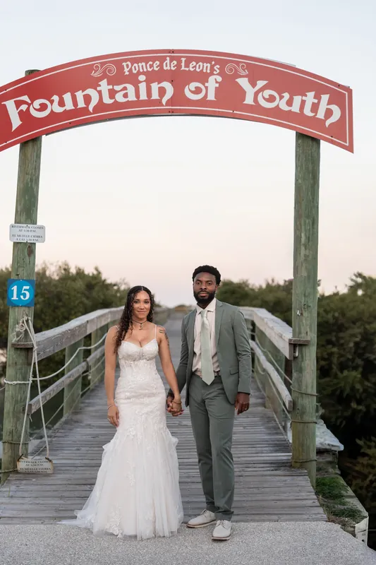 Lena and Blake walk hand-in-hand beneath the iconic Fountain of Youth sign, marking the entrance to the historic park.