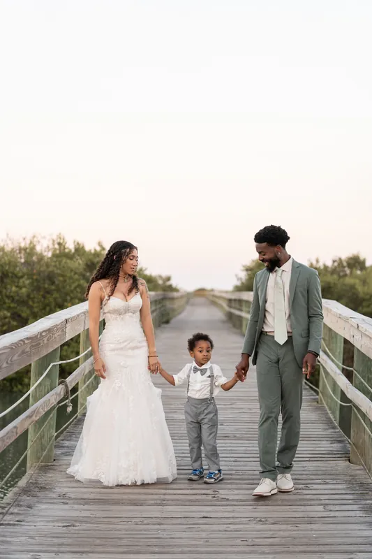Blake holds their young son's hand while walking with Lena across the wooden boardwalk at Fountain of Youth Archaeological