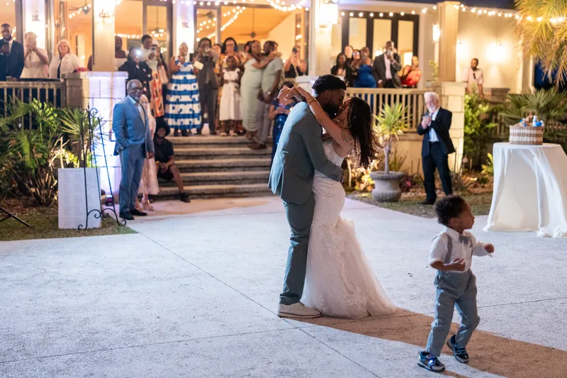 Blake and Lena dance together under string lights strung across the outdoor venue as guests watch from the illuminated