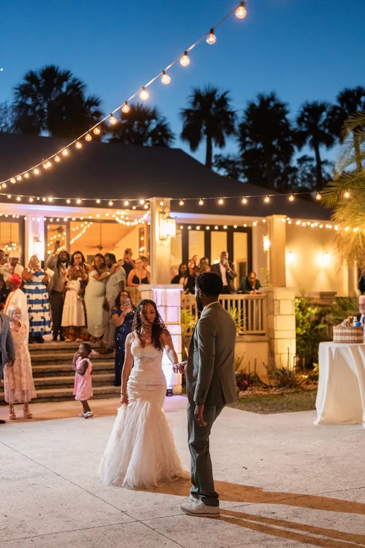 Palm trees silhouette against the evening sky as Lena and Blake slow dance under glowing string lights at the reception.