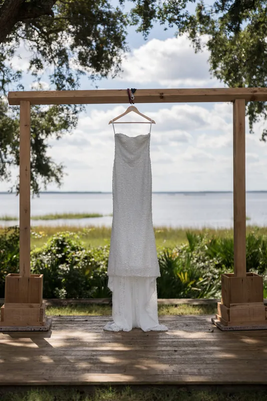 A white wedding gown hangs from a wooden pergola overlooking the river at The Preserve at Amelia River Club.