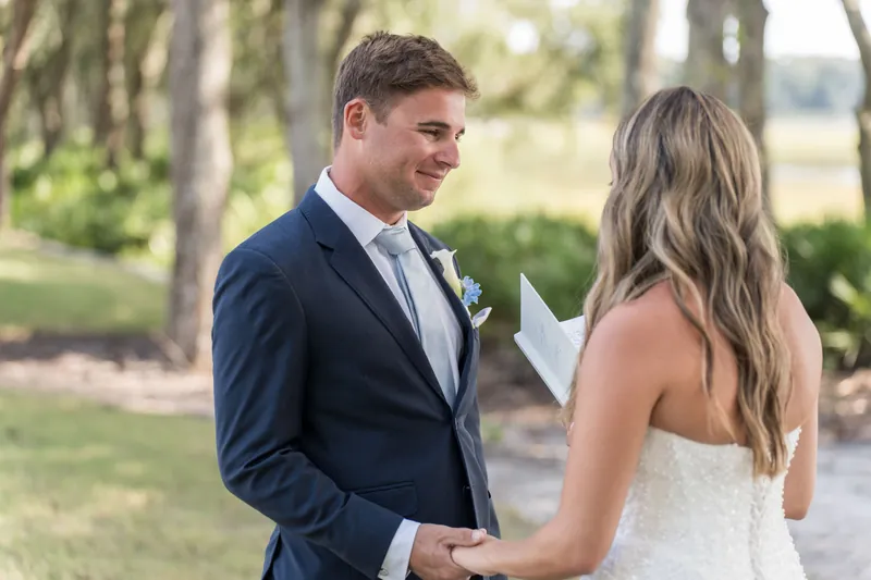 Lexie & Ed hold hands during their first look beneath the oak trees, both smiling at The Preserve at Amelia River Club.
