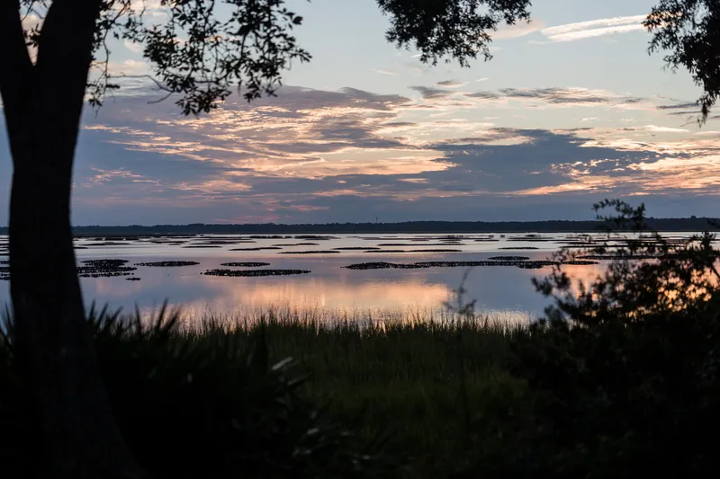 Sunset light paints the sky pink and purple over a river lined with marsh grasses and trees at The Preserve at Amelia River Club.