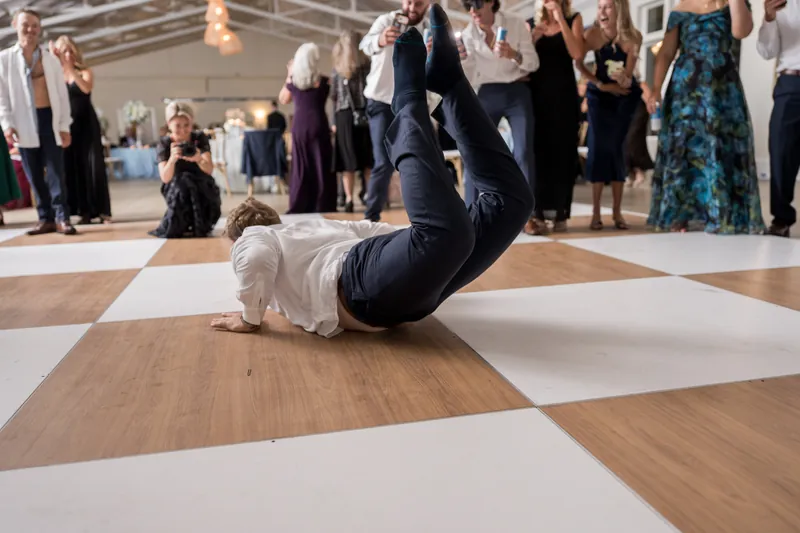 Someone in a white jacket performs a dramatic backbend on the dance floor while guests encircle the action.