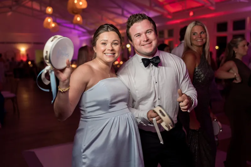 Two people dance at their reception in purple-lit surroundings, one in a pale blue strapless gown, the other in a tuxedo with bow tie.
