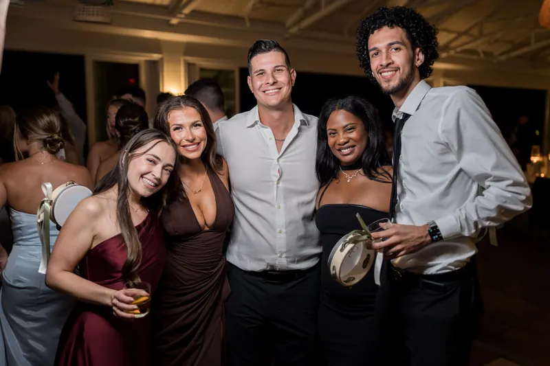 Five guests pose together at the reception, holding cocktails and smiling at the camera under warm indoor lighting.