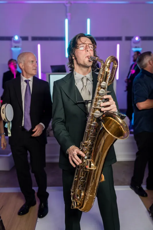 A saxophonist in a dark suit plays during the reception beneath purple neon lighting, with guests mingling nearby.