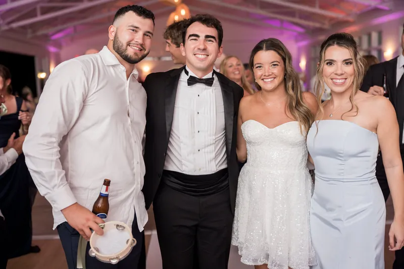 Two men and two women stand together for a photo at the reception; the woman on the left wears a white dress, the others in formal attire.