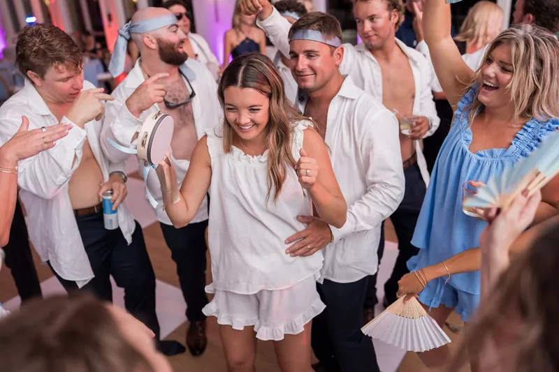 Guests in white and blue attire celebrate together on the dance floor, smiling and moving to music.