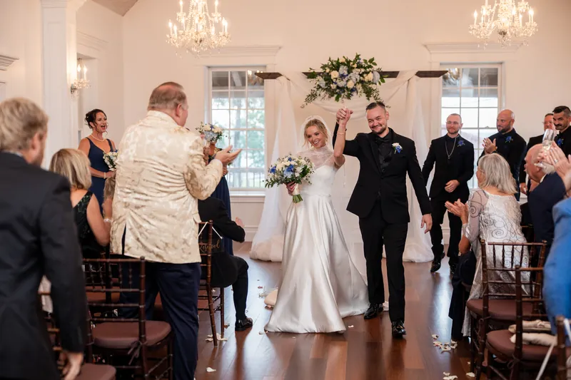 A couple in wedding dress and dark suit dances as guests watch from chairs lining both sides of a vaulted chapel aisle.