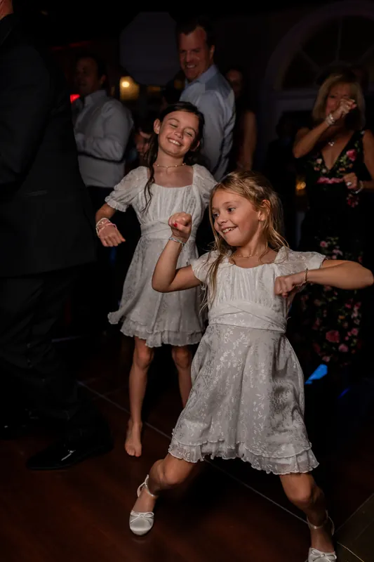 Young children dance together on the reception floor as adults celebrate around them under warm string lights.