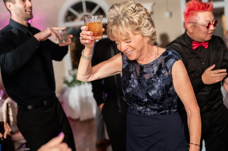 A woman in a dark sequined dress raises her glass in a toast, flanked by men in formal wear at the reception.