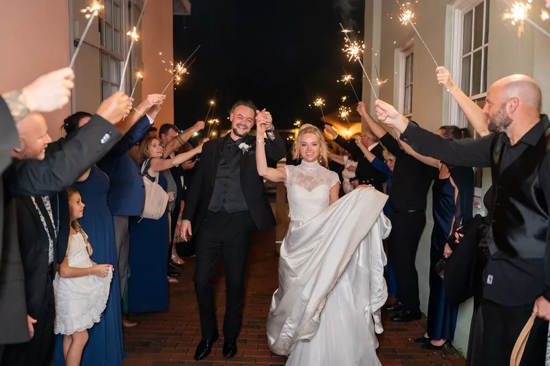 Li and Cody walk through a tunnel of sparklers held by guests in formal attire on an outdoor pathway at night.