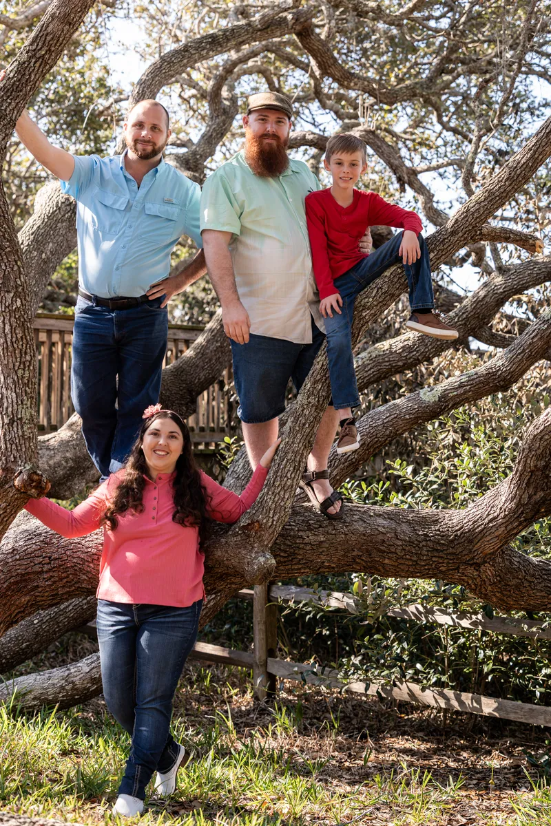 Family of four posing together in the oak tree branches at Nease Park
