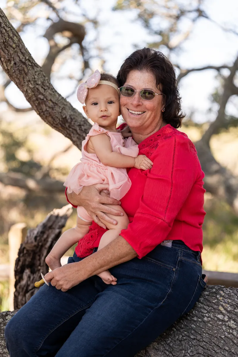Grandmother holding baby granddaughter on an oak tree branch
