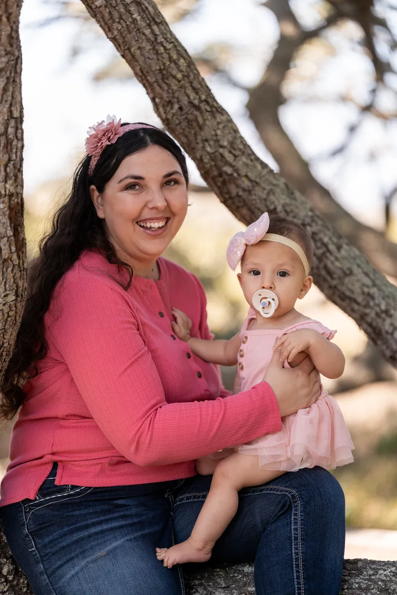 Mom smiling with baby daughter on her lap under the oak trees
