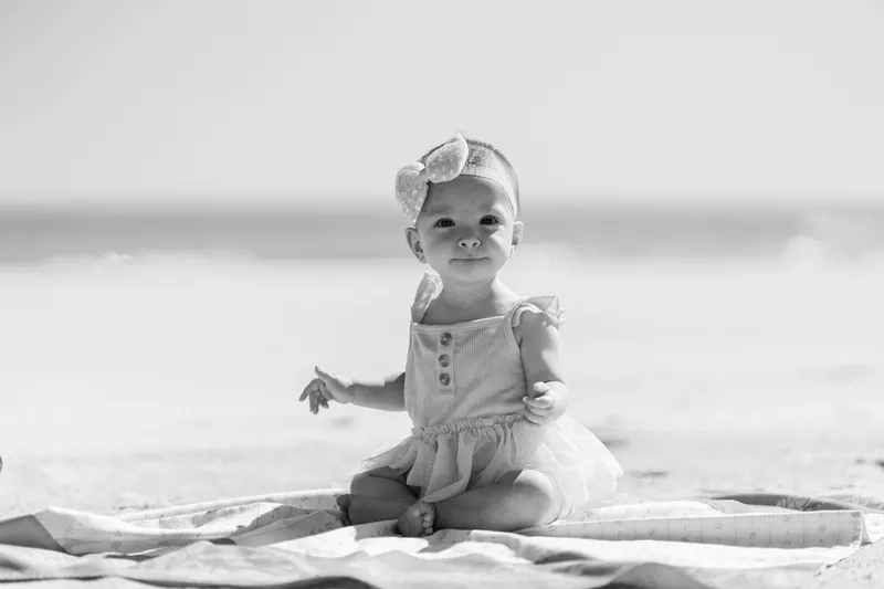 Black and white portrait of baby girl sitting on a blanket at the beach