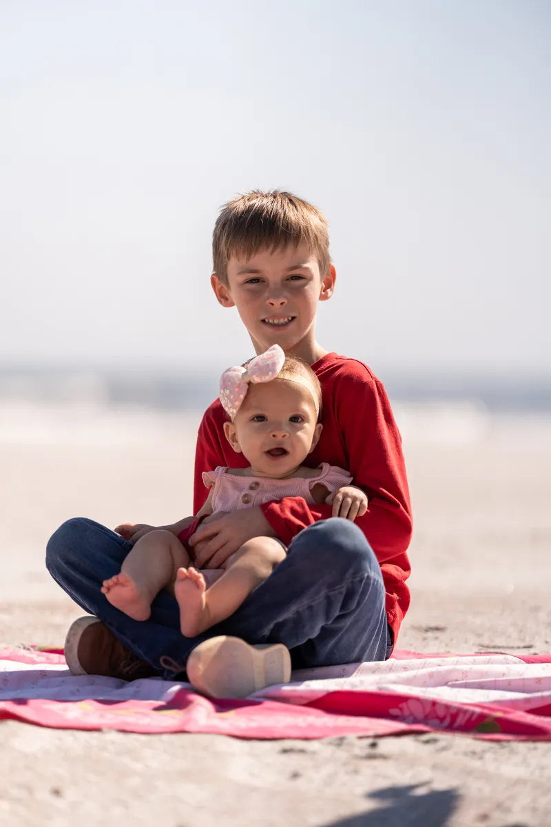 Big brother holding baby sister on a blanket at Vilano Beach