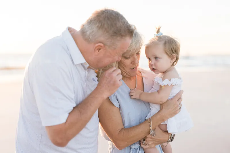 Two adults lean in close to kiss a toddler they're holding between them on the shoreline at Vilano Beach.