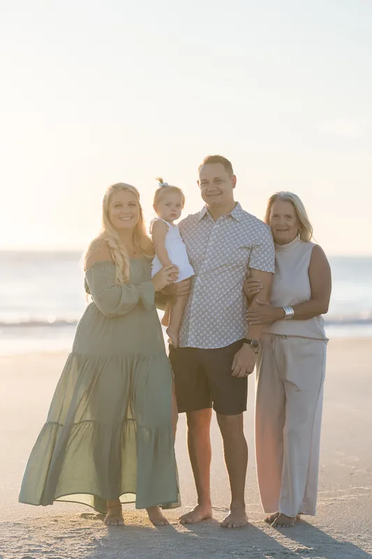 Four people stand together on Vilano Beach at sunset, with soft golden light behind them and calm ocean waves in the distance.