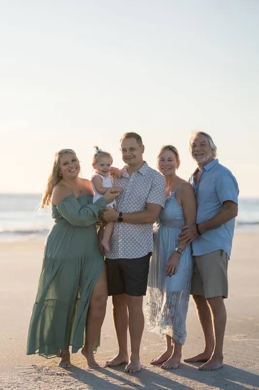 Five family members pose together on the sand at Vilano Beach, dressed in coordinating pastels and blues under clear skies.