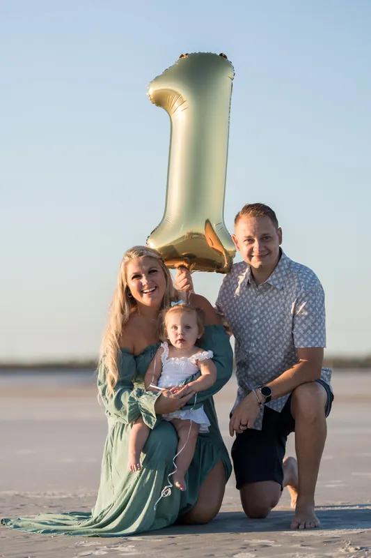 Two adults and two children crouch on wet sand beneath an oversized gold "1" balloon at Vilano Beach.