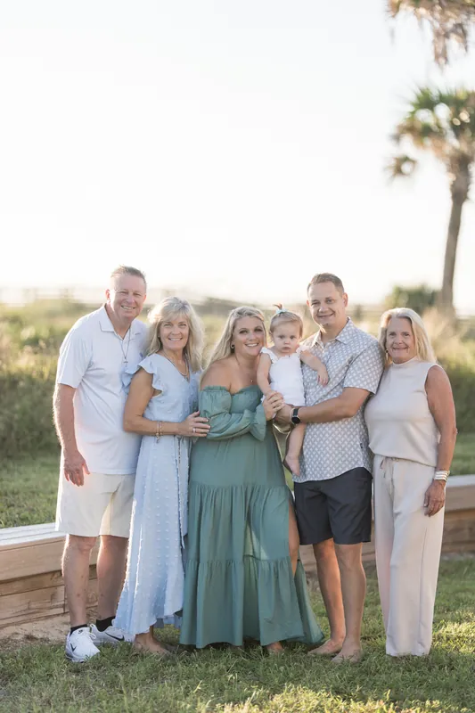 Seven family members stand together on a wooden deck at Vilano Beach with palms and water behind them.
