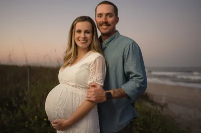 Couple holding hands during maternity session with sea oats and ocean waves behind them at Vilano Beach.