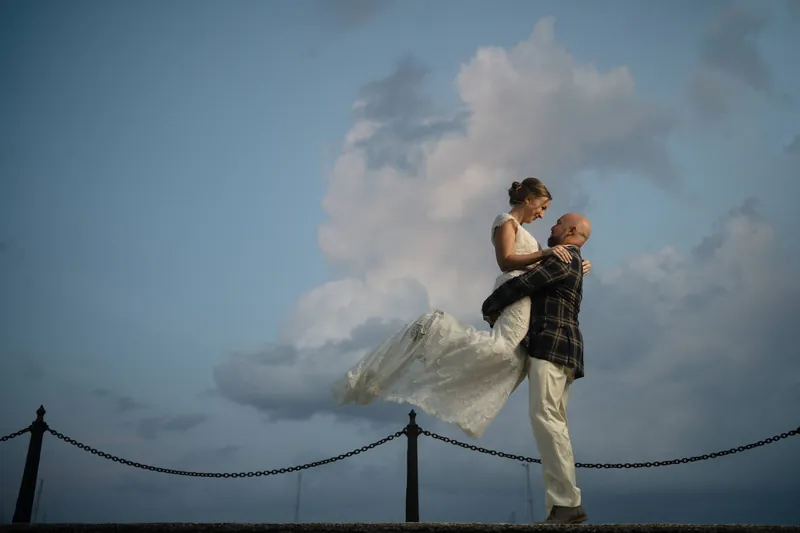 Groom lifting bride against sunset sky