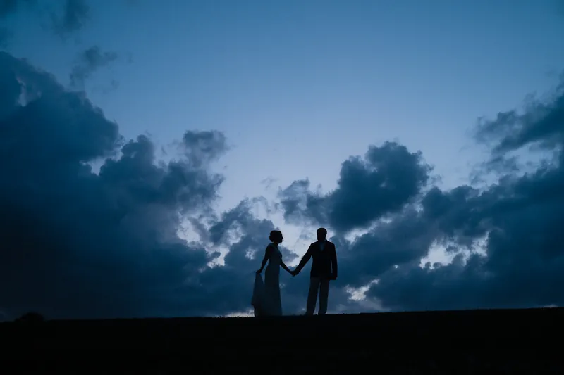Blue hour silhouette of couple holding hands against dramatic clouds