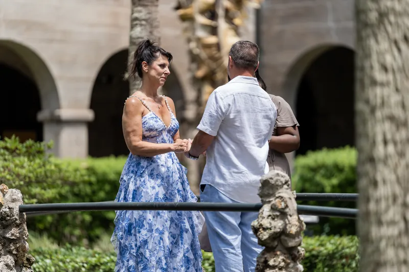 Mary and Brian hold hands while standing at a stone railing with The Lightner Museum's arched colonnades visible behind them.
