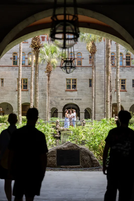 Silhouetted guests watch Mary and Brian exchange vows in The Lightner Museum's open-air courtyard beneath a hanging lantern.