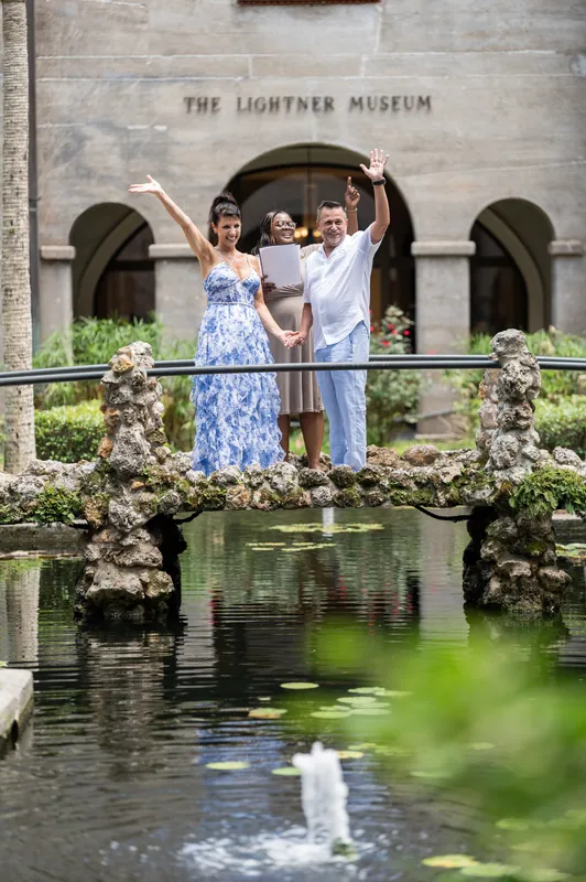 Mary and Brian raise their hands in celebration on the moss-covered bridge at The Lightner Museum.