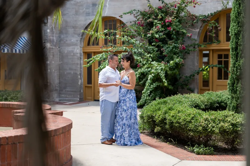 Mary and Brian embrace in a courtyard with ivy-covered walls and arched doorways behind them.