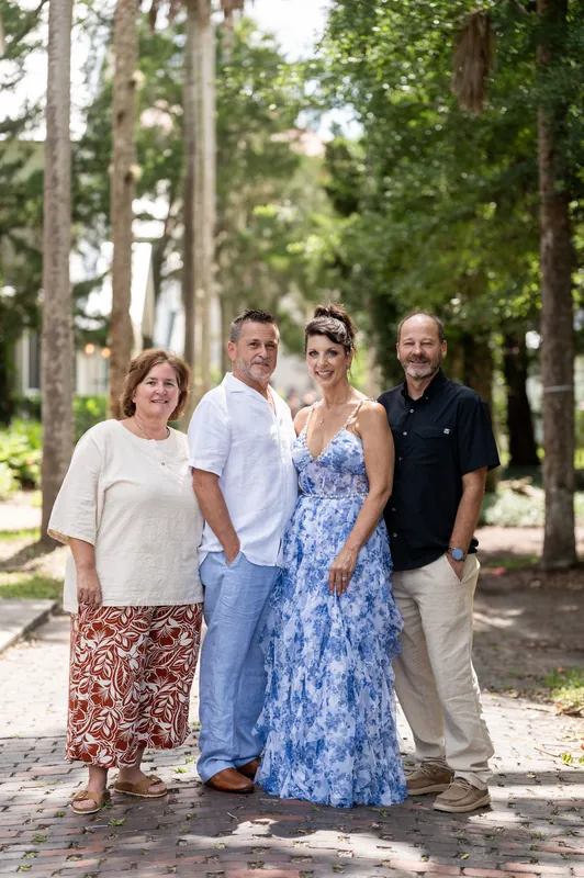 Mary and Brian stand with family members on a tree-lined brick pathway, dressed casually for their elopement celebration.